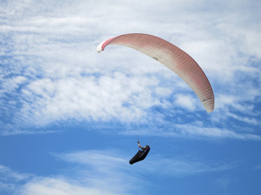 Gleitschirmflieger unter rot-weißem Schirm am Himmel